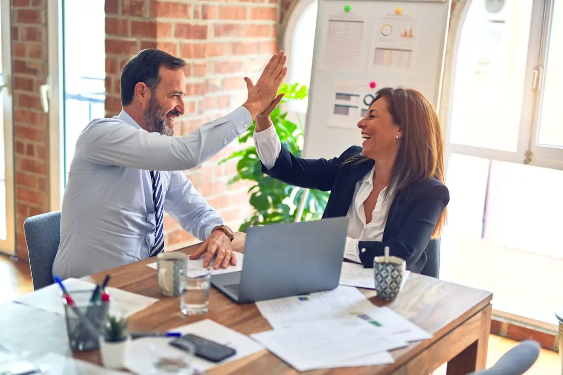 Dois profissionais comemorando com um high five durante uma reunião de trabalho