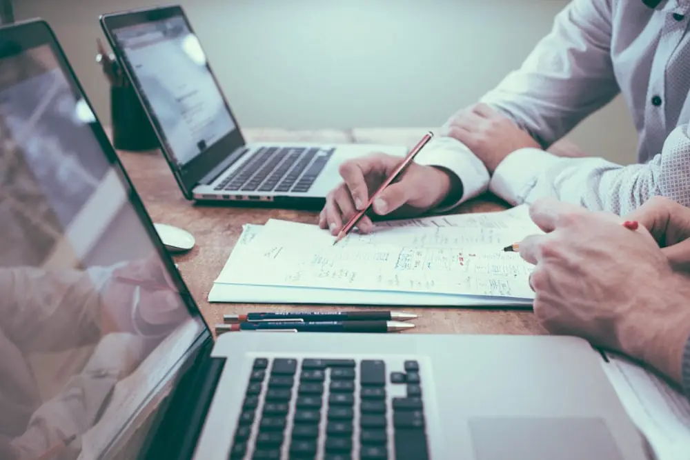 Mãos fazendo anotações ao lado de um notebook durante a análise de operações financeiras